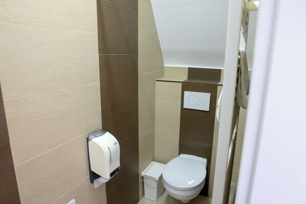 Un baño pequeño y moderno con inodoro, un cesto de basura y dispensador de toallas de papel.