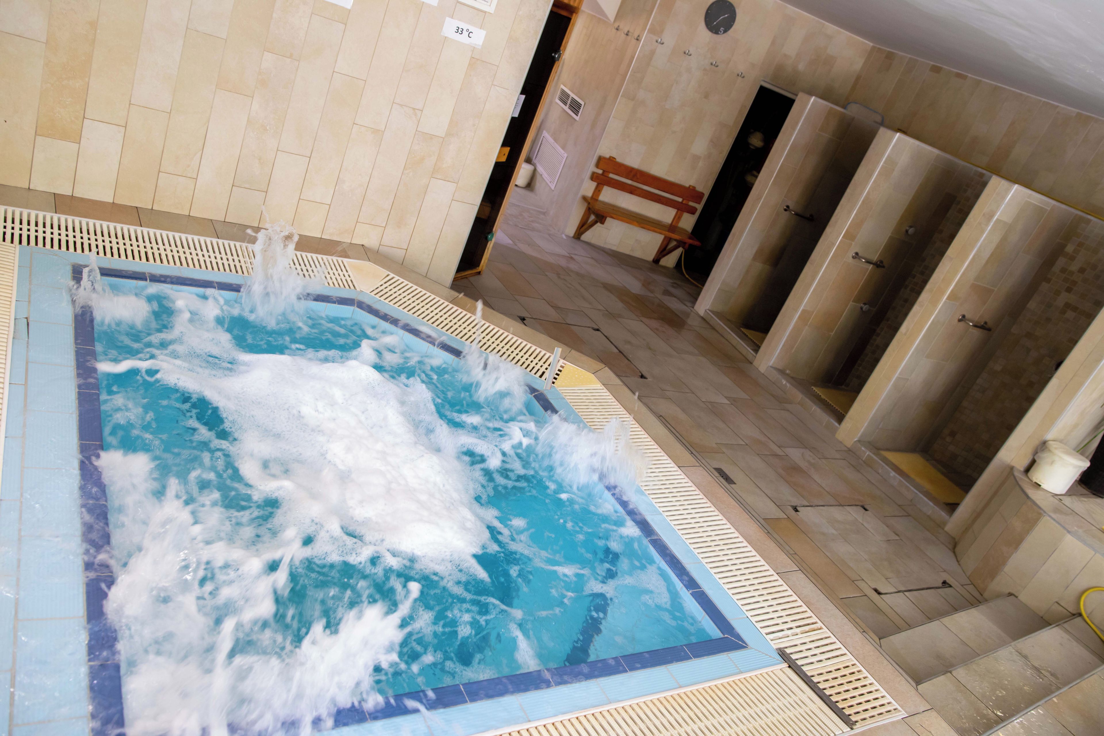A hot tub with water jets, a wooden bench, and a tiled floor.
