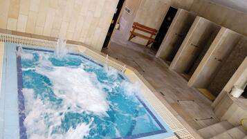 A hot tub with water jets, a wooden bench, and a tiled floor.