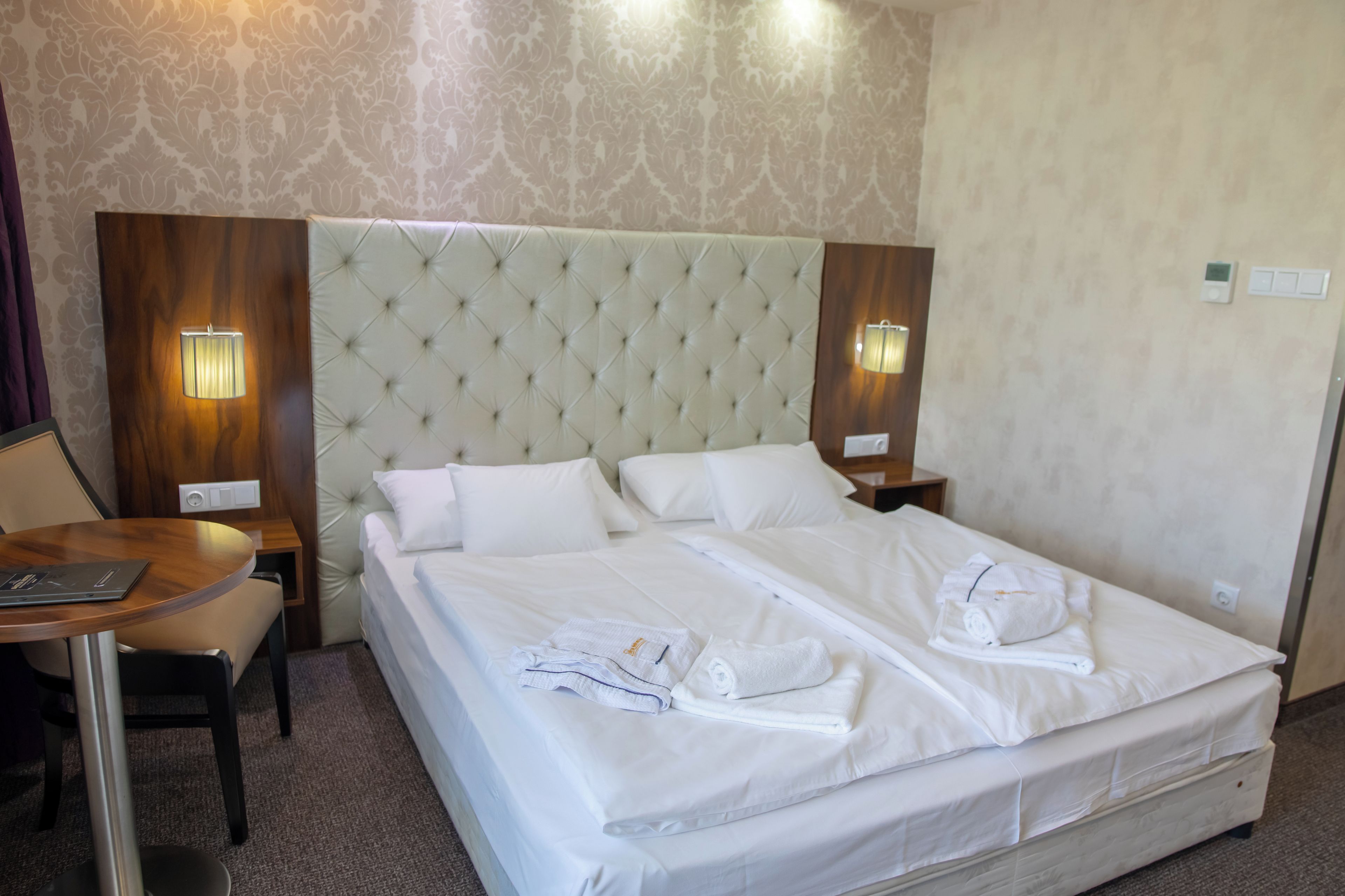 Quarto de hotel com uma cama grande, duas mesas de cabeceira, uma escrivaninha e uma cadeira.