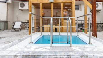 An indoor swimming pool with a wooden deck and a glass enclosure.