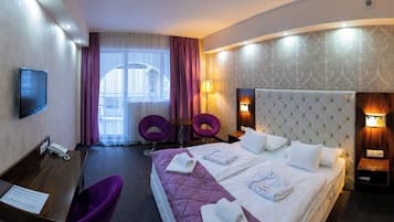 A hotel room with a large bed, two purple chairs, a desk with a phone, and a TV.