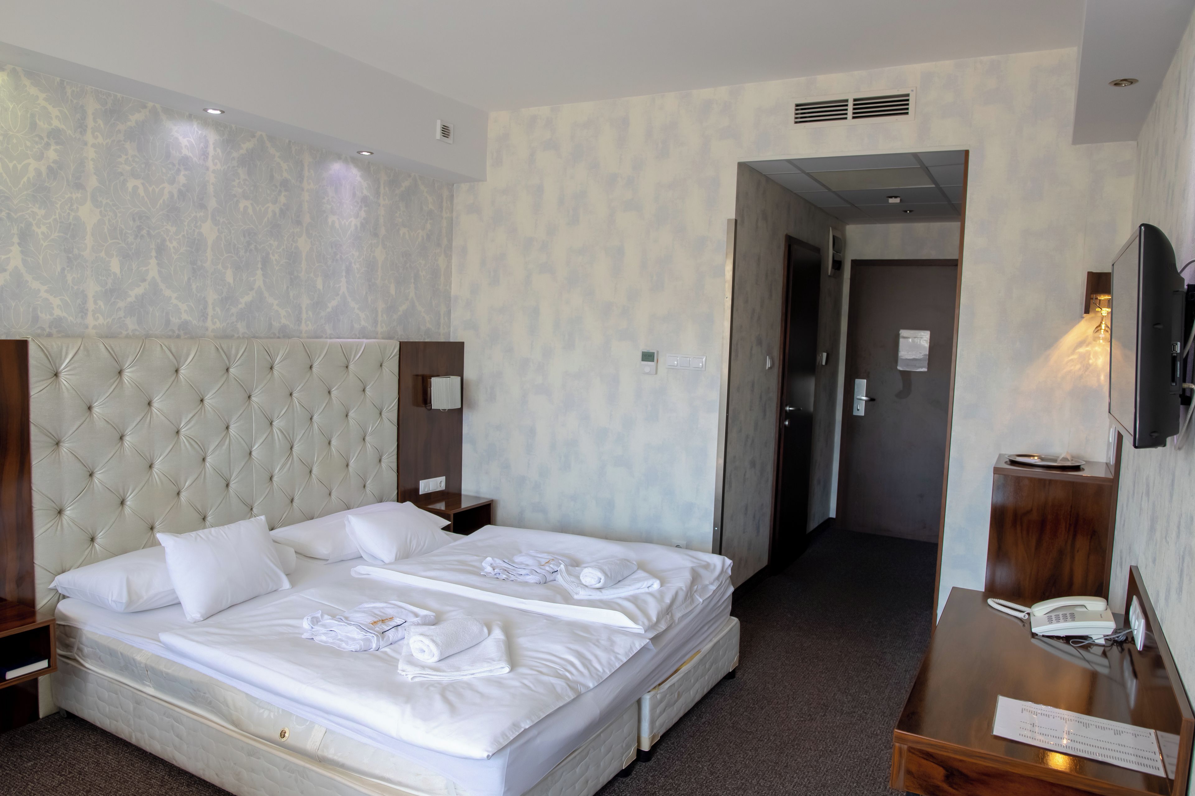 A hotel room with a large bed, a wooden nightstand, a desk with a telephone, and a television.