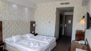A hotel room with a large bed, a wooden nightstand, a desk with a telephone, and a television.