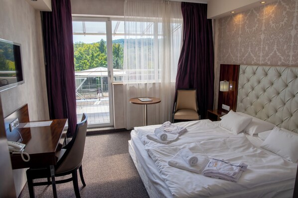 Habitación de hotel con cama, escritorio, silla, mesita y televisor.