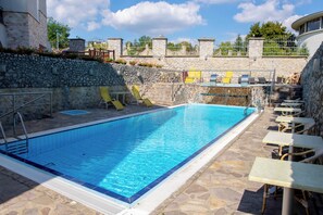 A swimming pool with a stone wall, lounge chairs, and a stone staircase leading to a deck area. - Bastya Wellness Hotel (Miskolc)