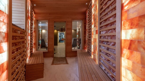 A corridor with wooden benches and a view into a room with exercise equipment. - Bastya Wellness Hotel (Miskolc)