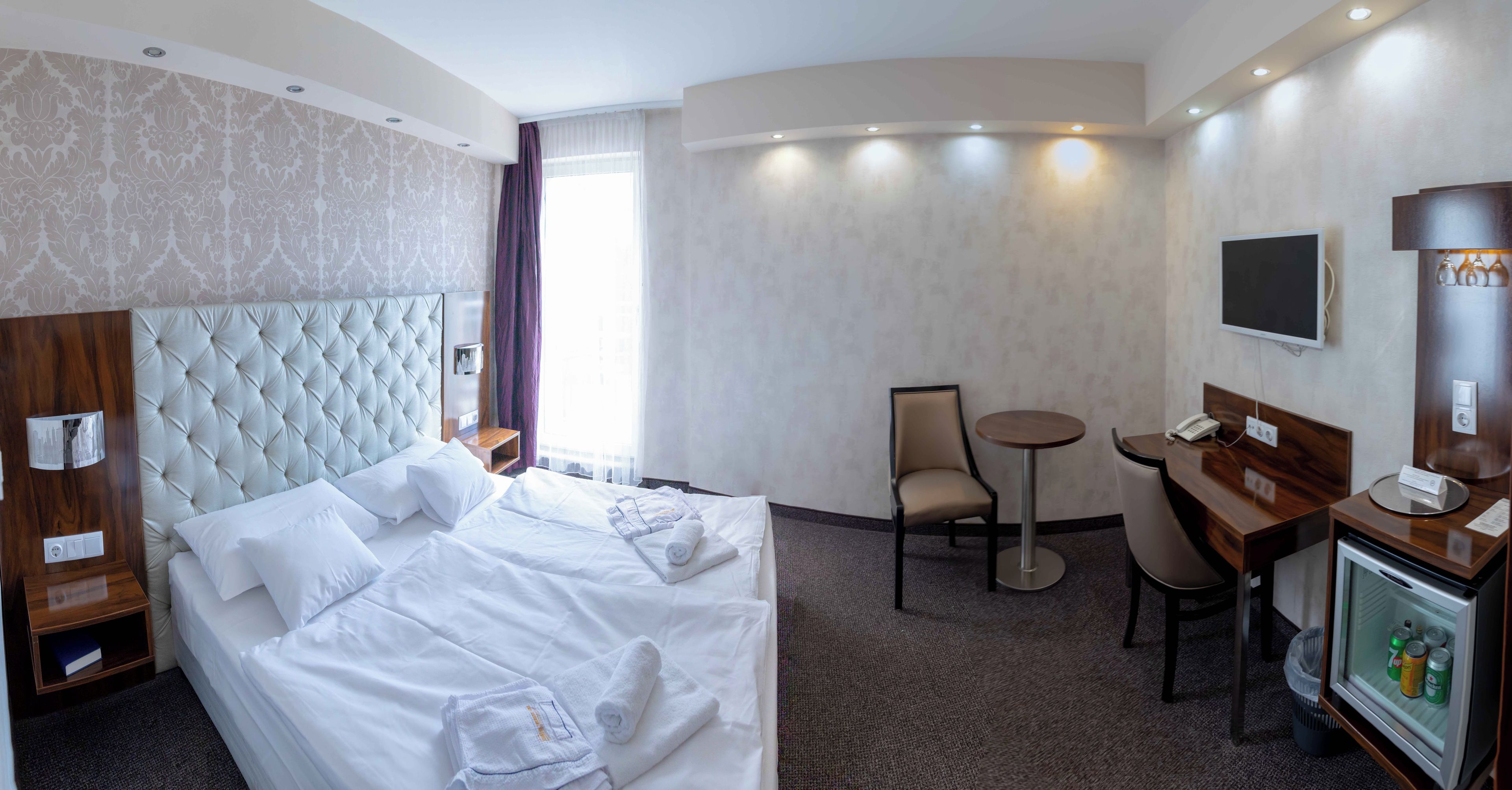 A hotel room with a large bed, a desk, a chair, a television, and a minibar.