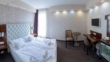 A hotel room with a large bed, a desk, a chair, a television, and a minibar.