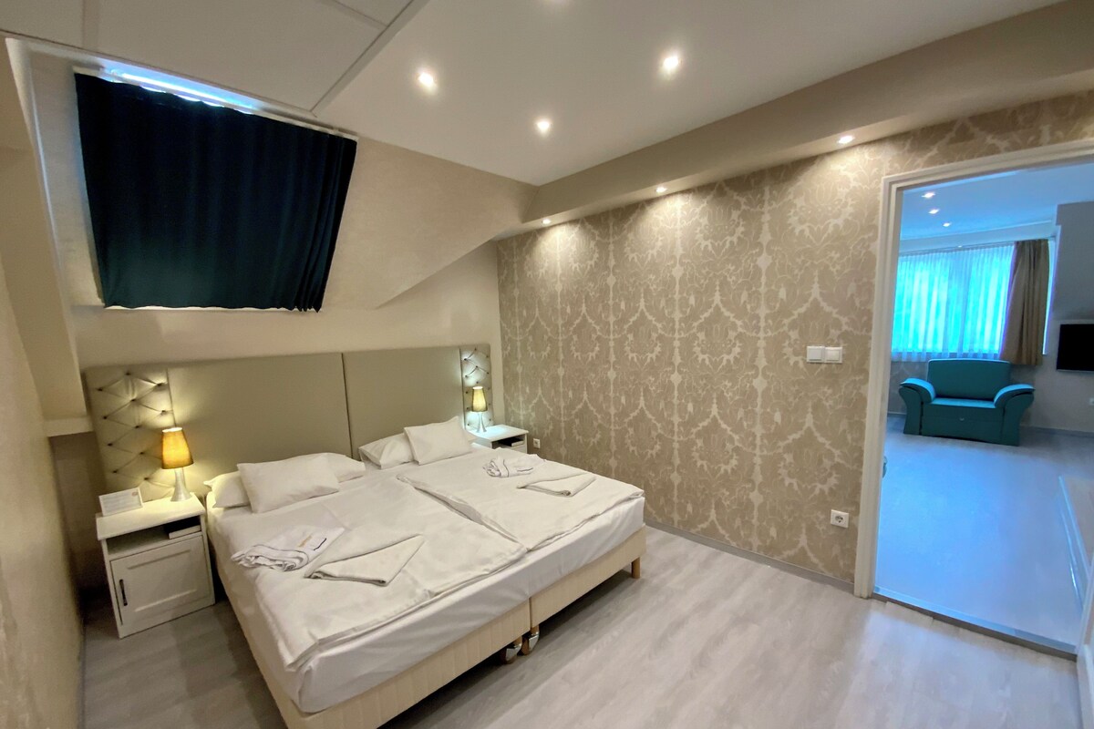 A modern hotel room with a large bed, bedside tables with lamps, a TV mounted on the wall, and a patterned wallpaper.