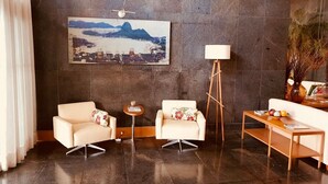 Un vestíbulo moderno con dos sofás, una lámpara de pie, una mesa con frutas y una pintura de un paisaje urbano en la pared.