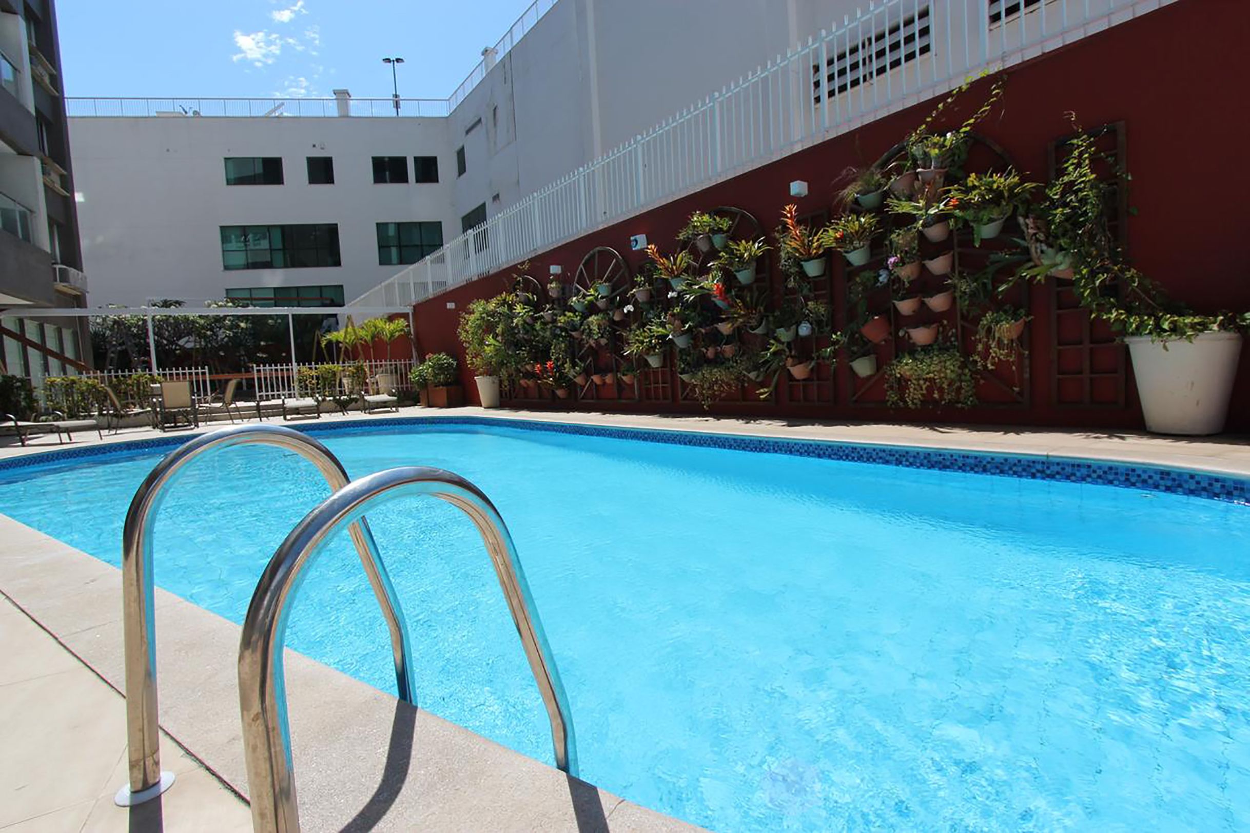 A swimming pool with metal railings, surrounded by a building with a red wall and potted plants.