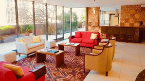 Un salón amplio con un sofá rojo, sillones blancos y una mesa de centro. Ventanas grandes ofrecen vistas al exterior.
