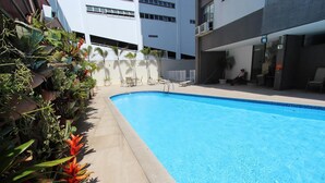 Una piscina con bordeado de baldosas, rodeada de macetas con plantas y sillas.