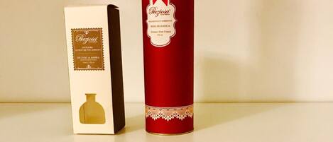 A shelf with a red cylindrical container labeled 'Preziosa' and a box with similar branding. Below, a box of scented candles and a bottle of reed diffuser are displayed.
