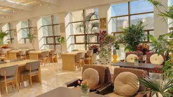Un amplio vestíbulo de hotel con varias zonas de estar, ventanas grandes y plantas de interior.