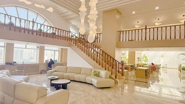 A spacious lobby with a high ceiling, a staircase, and a seating area with sofas and tables. - Haolong Hotel (Xining)