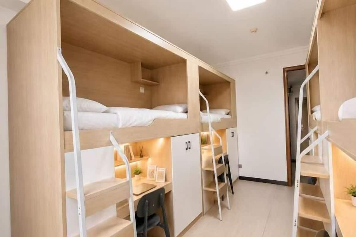 Une chambre de dortoir équipée de lits superposés, de bureaux, de chaises et d’une petite bibliothèque.