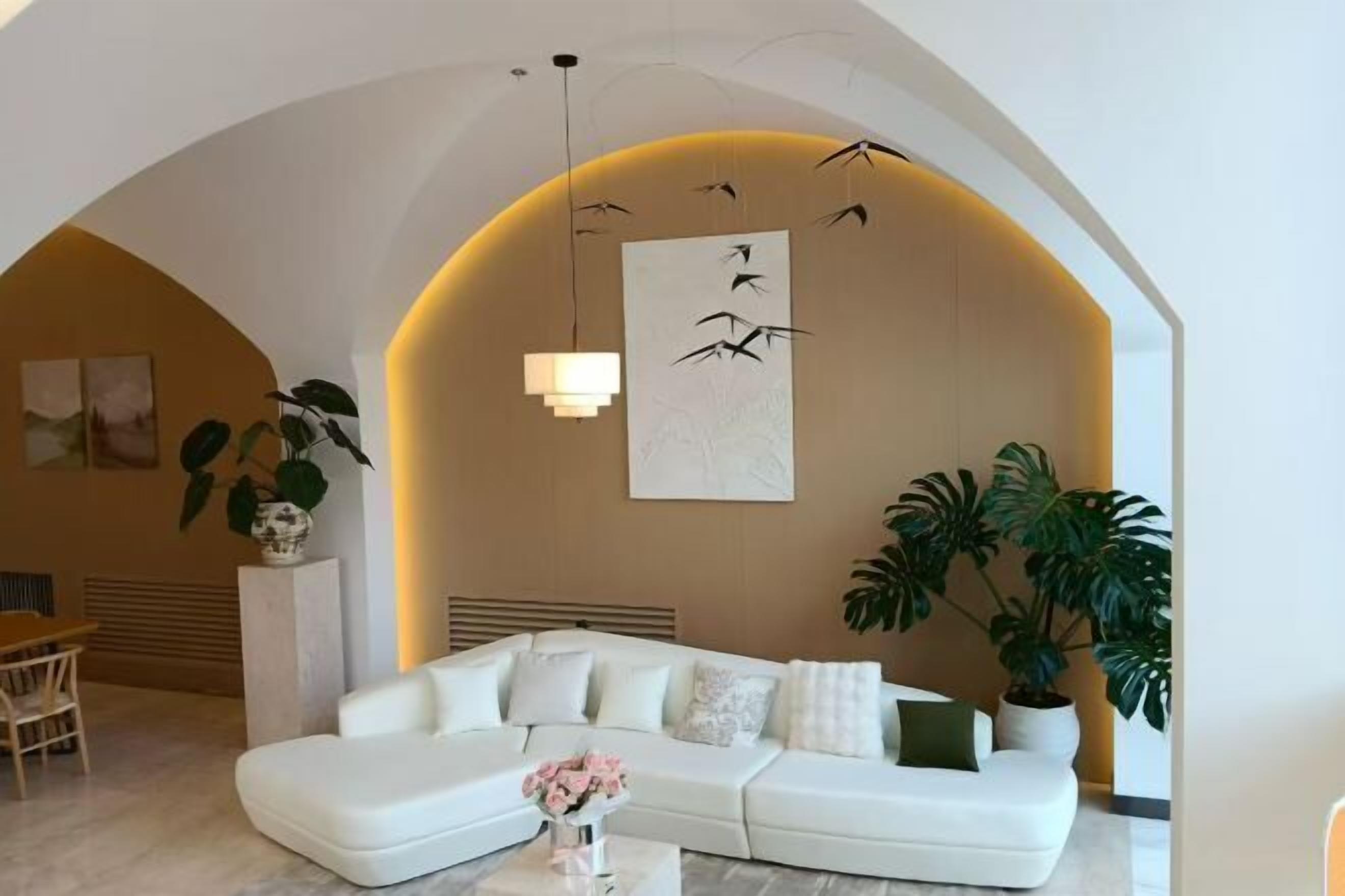 Una sala de estar moderna con un sofá blanco, una mesa de centro con flores y plantas grandes.