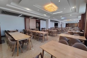 A spacious dining area with multiple tables and chairs, a modern ceiling design, and a neutral color palette.