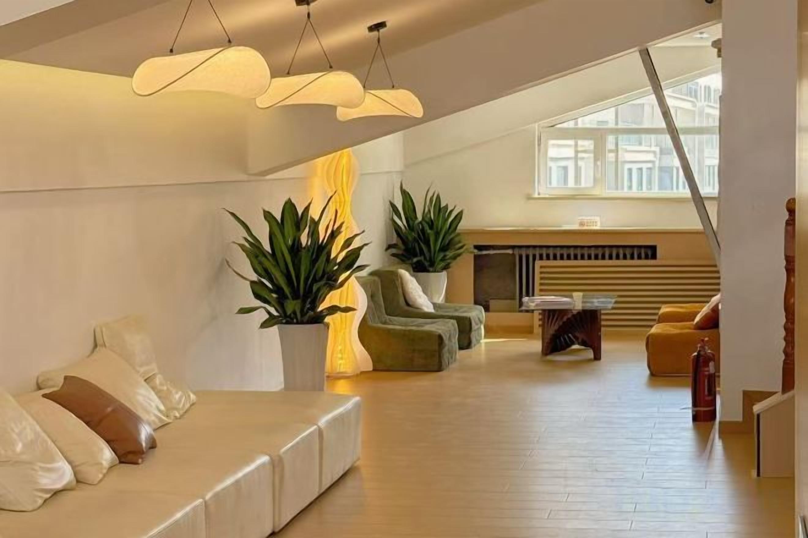 Un salón amplio con techo alto, un conjunto de sofás, una mesa de centro y dos plantas en macetas.