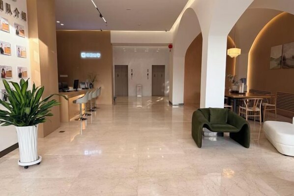 A hotel lobby with a reception desk, seating area, and a large potted plant.