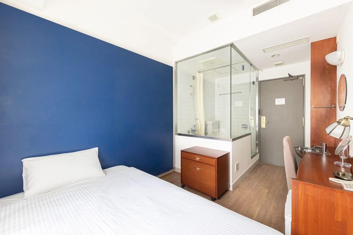 Habitación de hotel con cama, escritorio, espejo y un separador de vidrio.