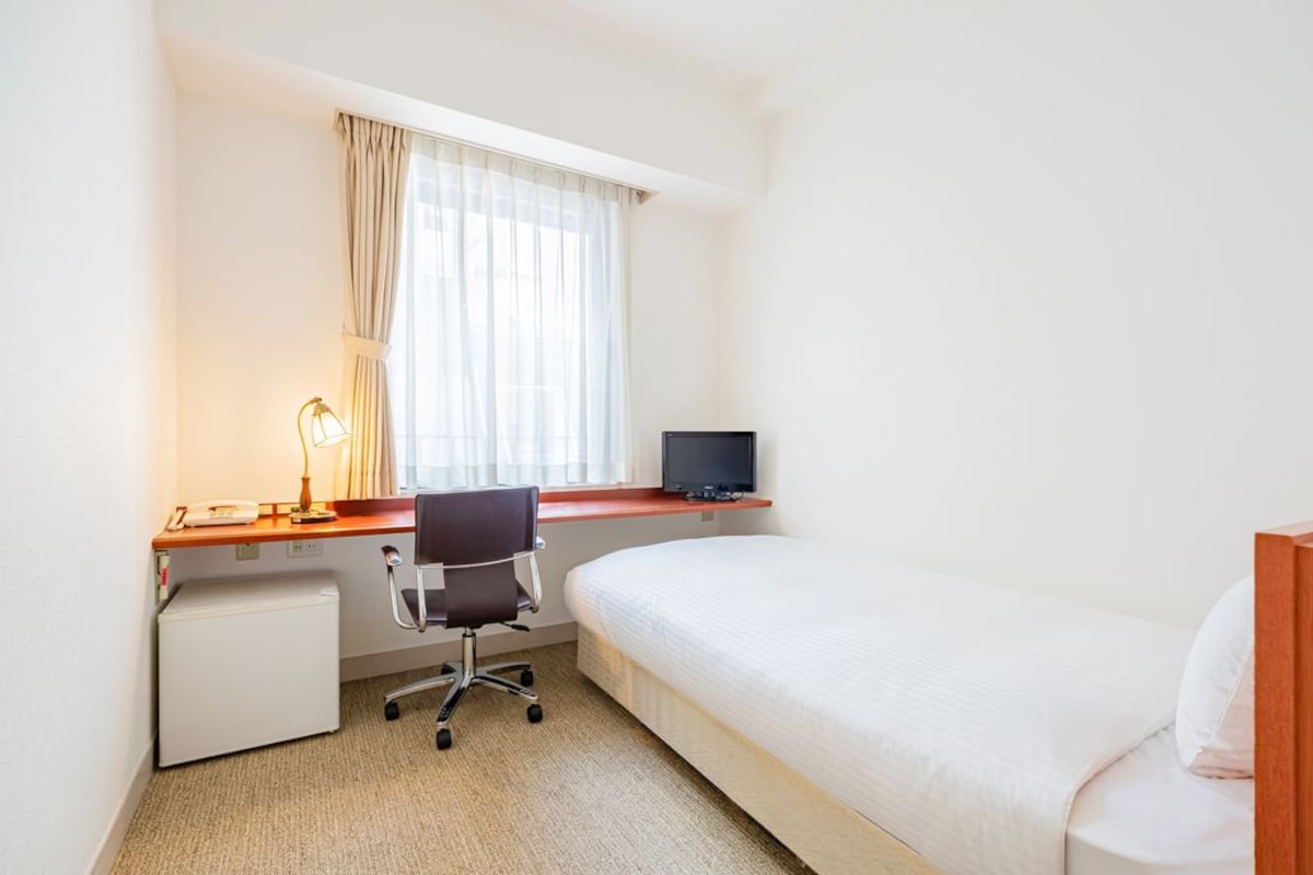 Habitación de hotel con cama, escritorio con computadora, silla y un refrigerador pequeño.