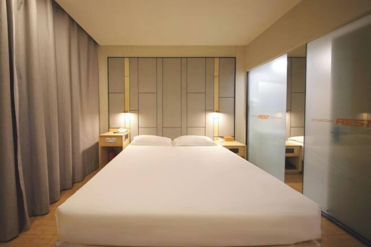 A hotel room with a large bed, two bedside tables, a nightstand, a mirror, and a sliding door.