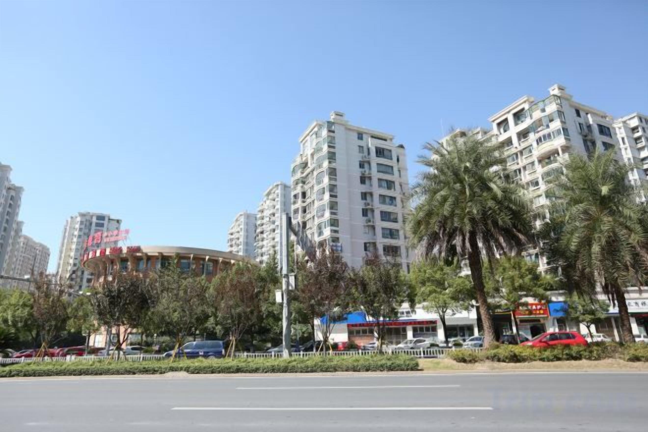 A city street with high-rise buildings, palm trees, and parked cars.