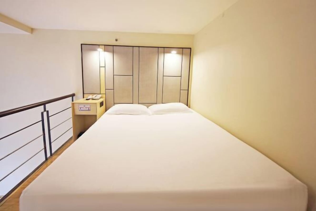 A hotel room with a bed, bedside table, and a nightstand with a phone.