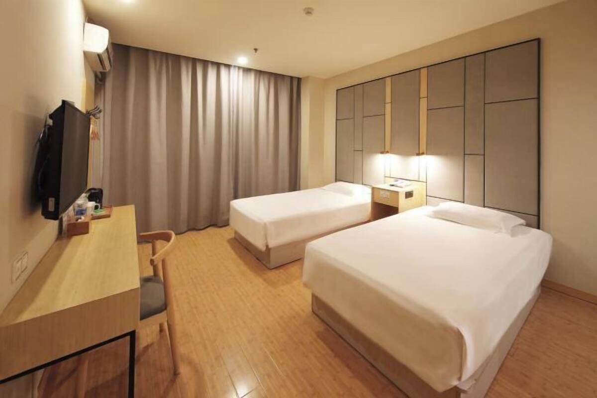 A hotel room with two beds, a desk, a chair, a TV, and a large mirror.