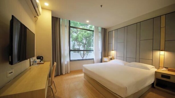 A hotel room with a bed, bedside tables, a desk with a flat-screen TV, a window with curtains, and an air conditioning unit. - Rest Motel (Xincheng Road) (WENZHOU)