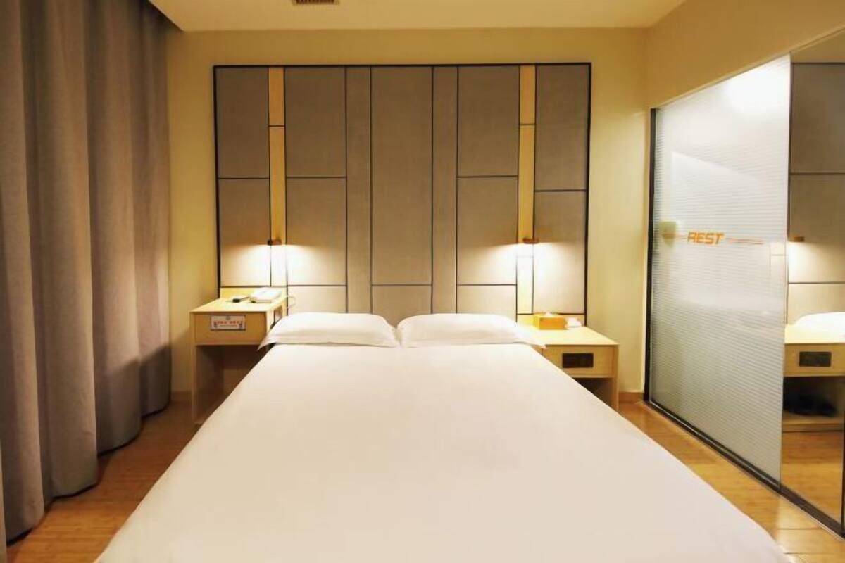 A hotel room with a large bed, two bedside tables with lamps, a sliding glass door, and a curtain on the left.