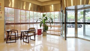 A modern lobby with a glass door entrance, a potted plant, and seating area with chairs and tables. - Rest Motel (Xincheng Road) (WENZHOU)