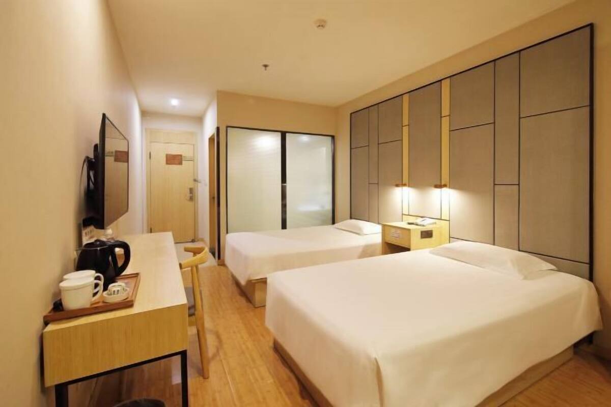 A hotel room with two beds, a desk with a coffee maker, a TV, and a sliding door.