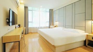 A hotel room with a large bed, a desk, a flat-screen TV, and a window with curtains.