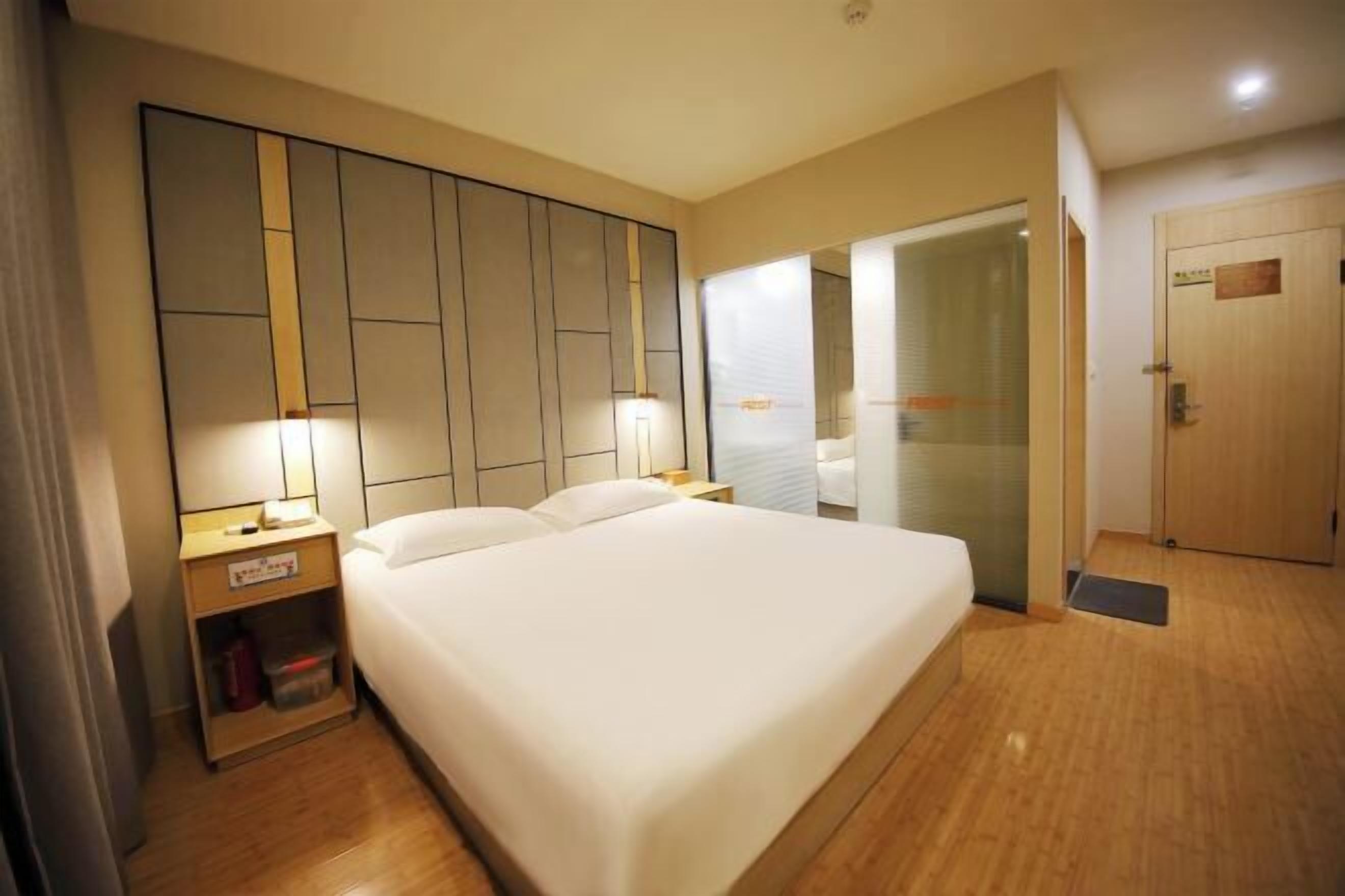 Una habitación de hotel con una cama grande, mesitas de noche, un armario y una puerta.