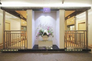 A reception area with a reception desk, a flower arrangement, and a sign indicating the entrance to the hotel. - Rest Motel (Xincheng Road) (WENZHOU)