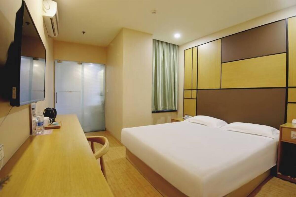 A hotel room with a bed, a desk, a chair, a television, and a window with curtains.
