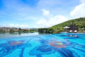 A swimming pool with a mosaic design, surrounded by lush greenery and a clear sky.