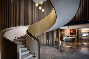 Eine moderne Hotelhalle mit einer geschwungenen Treppe, einer Rezeption und einem polierten Marmorboden.