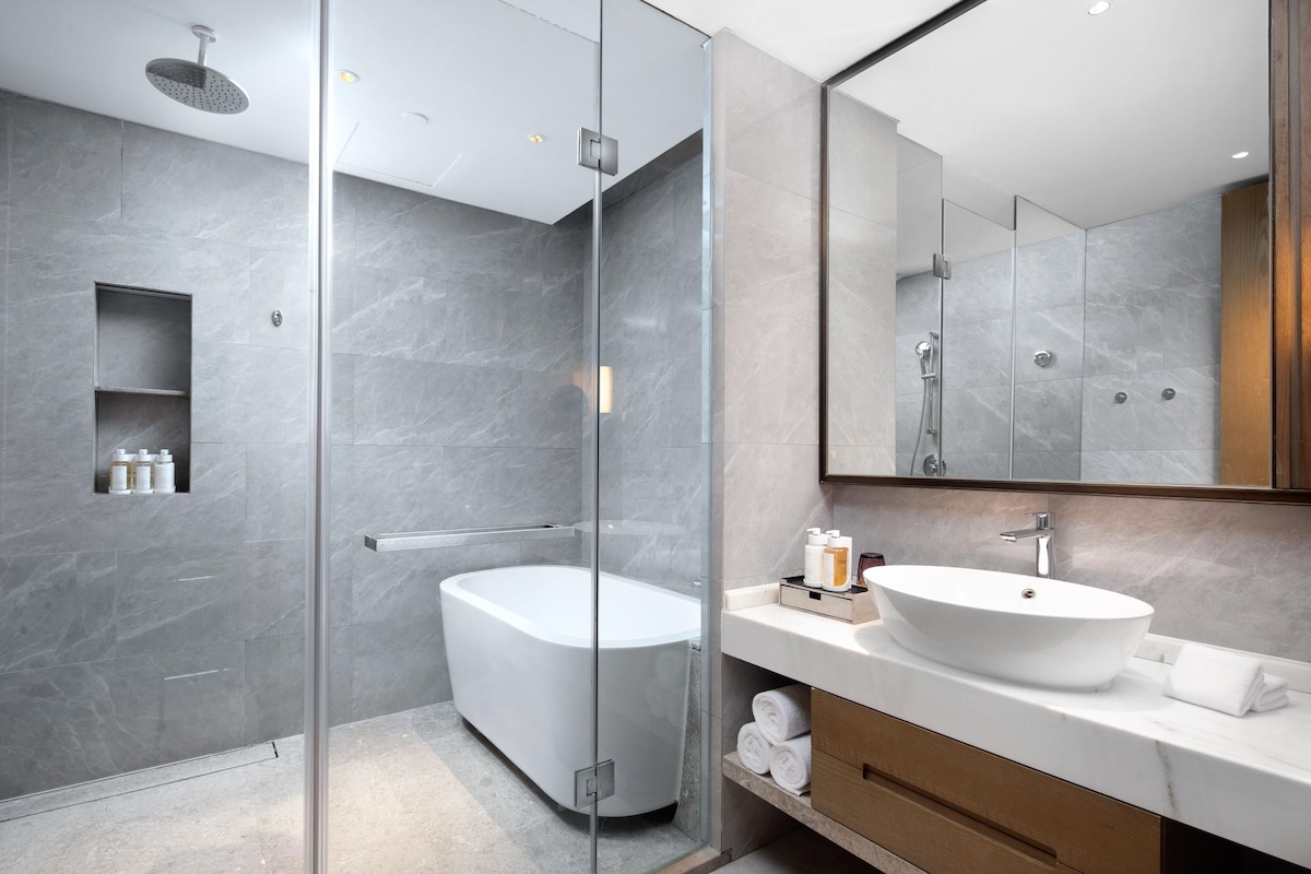 Ein modernes Badezimmer mit einer gläsernen Duschkabine, einer freistehenden Badewanne und einem Waschtisch mit großem Spiegel.