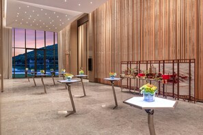 Un moderno vestíbulo de hotel con un amplio ventanal que ofrece una vista panorámica, varias mesas con centros de flores y una pared decorativa con elementos verticales.