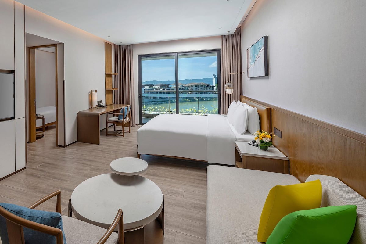 A hotel room with a bed, a desk, a TV, a round table, and a view of the city.