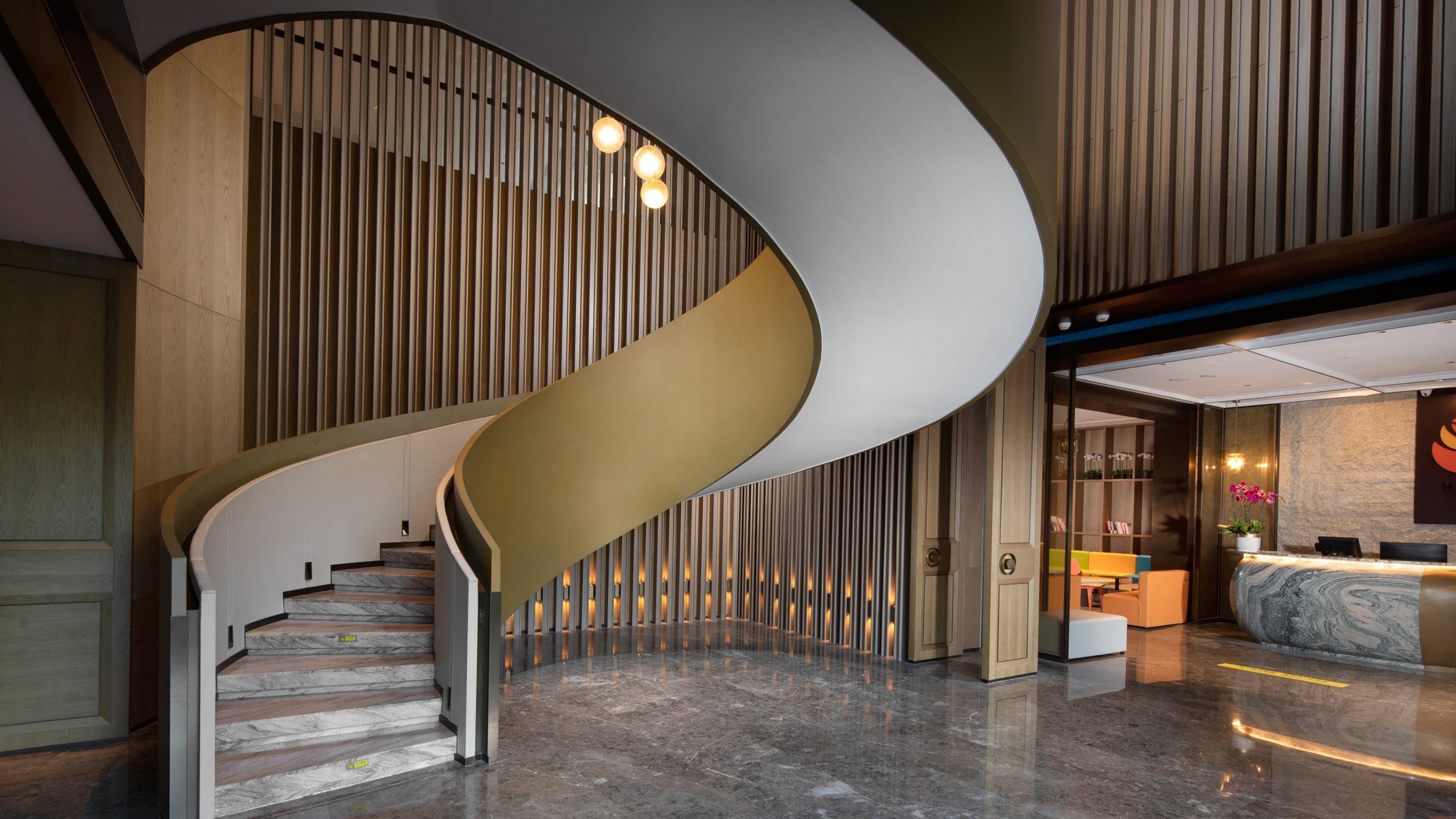 A modern hotel lobby with a curved staircase, a reception desk, and a seating area.
