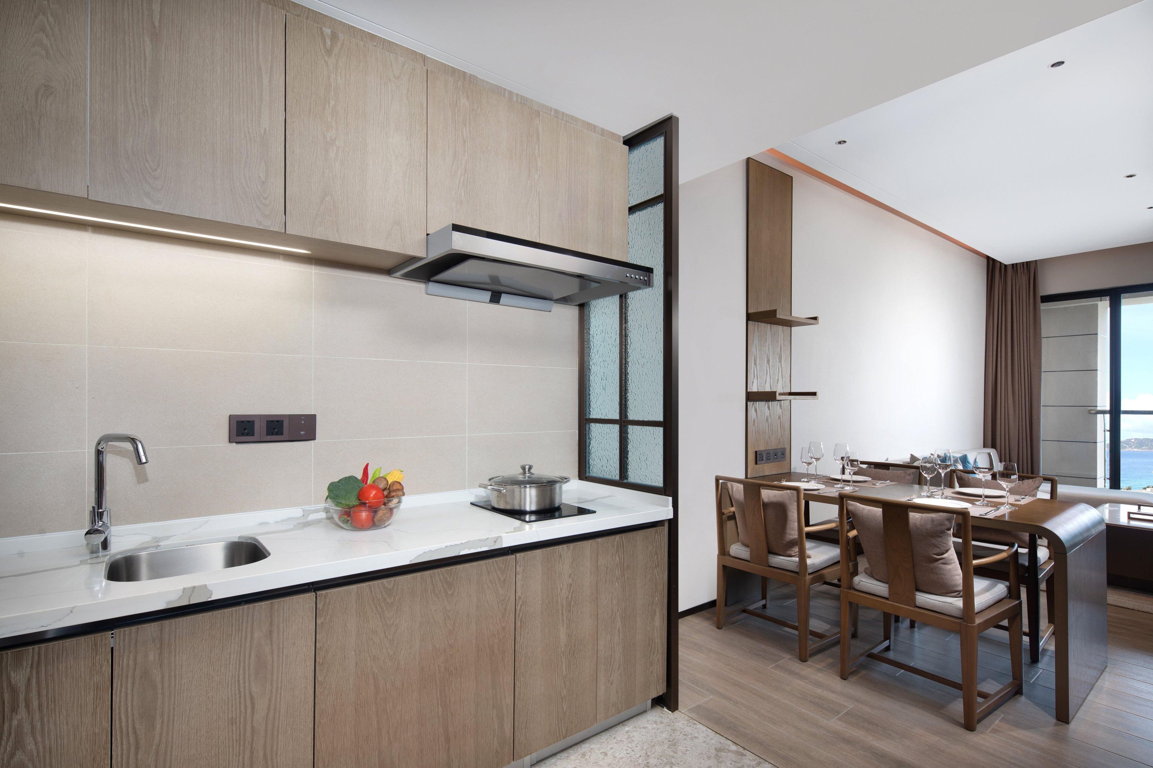 A modern kitchen with a built-in stove, a sink, and a dining area with wooden chairs and a table.
