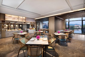 A modern dining area with tables and chairs, a counter with a display, and a view of the cityscape through large windows.