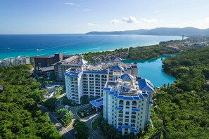 Un hotel moderno de gran altura con varios balcones con vistas a la costa, aguas azules cristalinas y un puente a lo lejos.