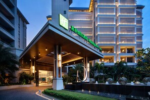 Entrada de un hotel Holiday Inn con un paseo techado, palmeras y un edificio grande al fondo.